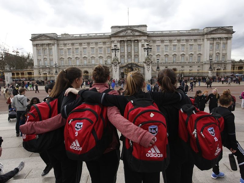 Group of teenage girls with red backpacks in front of Buckingham Palace