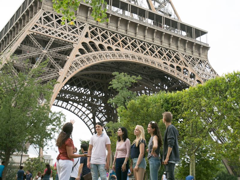 A group of young adults and an adult admire the Eiffel Tower, an iconic metal structure in Paris, France.