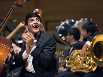 Young musician in tuxedo clapping in front of a double bass at an orchestra concert