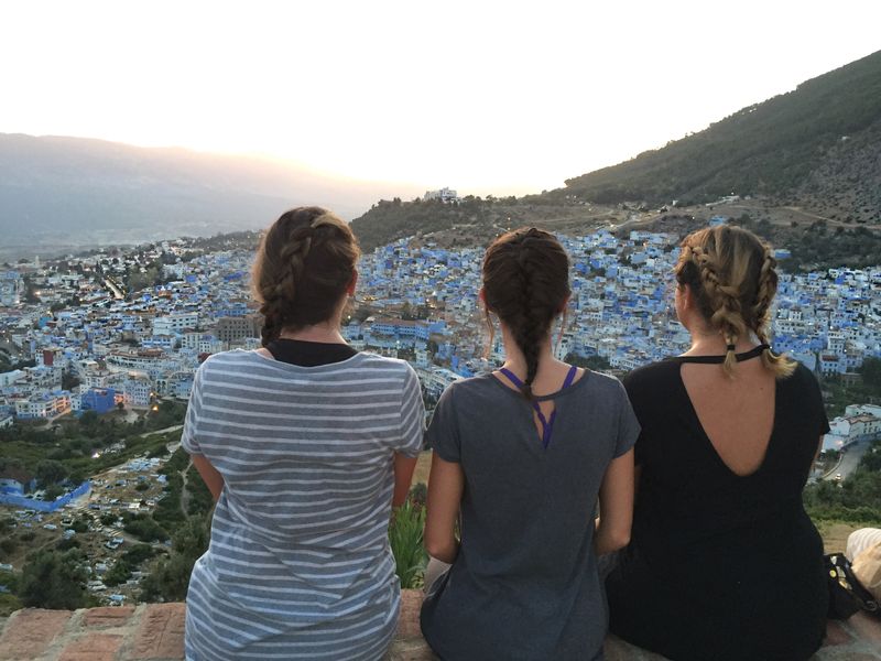 Three young adults gaze at the blue-washed buildings of Chefchaouen, Morocco during sunset.