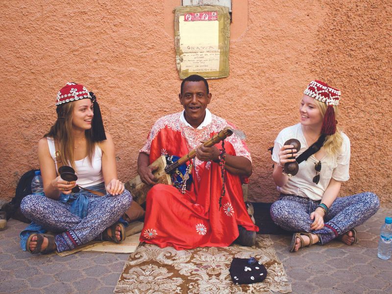 Two women and a Gnawa musician create music together on a Moroccan street.