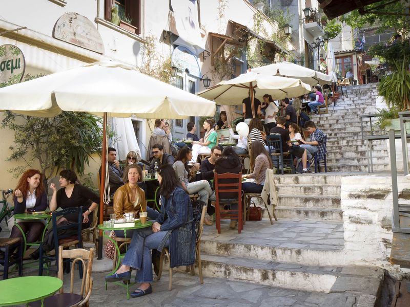 People enjoy a sunny day at an outdoor cafe on a stepped street in Athens, Greece.