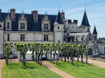 A scenic view of a French château and its gardens, overlooking a river and a bridge under a sunny sky.