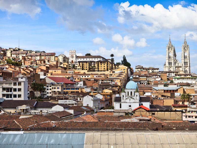 Panoramic view of a South American city with a mix of architectural styles, highlighted by a white church with a blue dome against a backdrop of a blue sky.