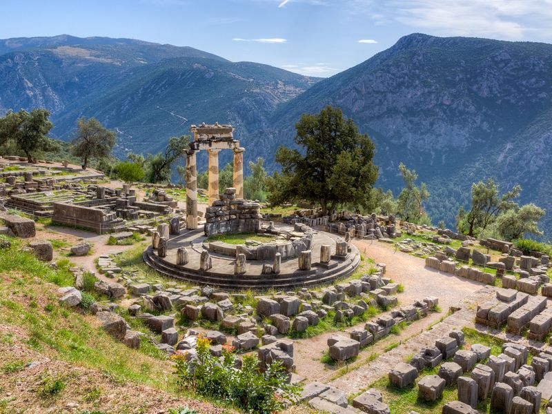 The ruins of the Tholos of Athena Pronoia in Delphi, Greece. The temple sits atop a hill, providing stunning views of the surrounding mountains.