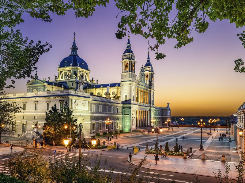 The Almudena Cathedral in Madrid, Spain, beautifully illuminated at sunset, with people strolling in the square.