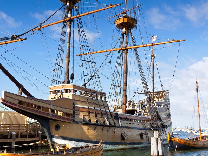 A large wooden sailing ship, reminiscent of the Mayflower II, docked at a pier in Boston.