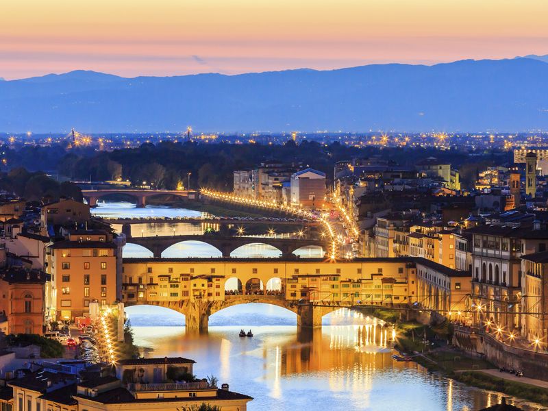 Scenic view of Florence at dusk, featuring the Ponte Vecchio illuminated over the Arno River.