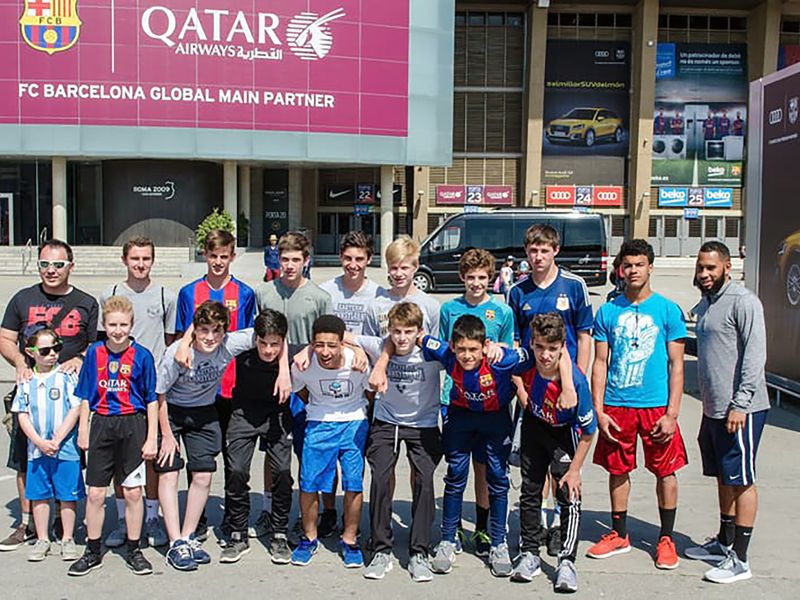 A youth soccer team poses for a photo in front of a sign at FC Barcelona's stadium.