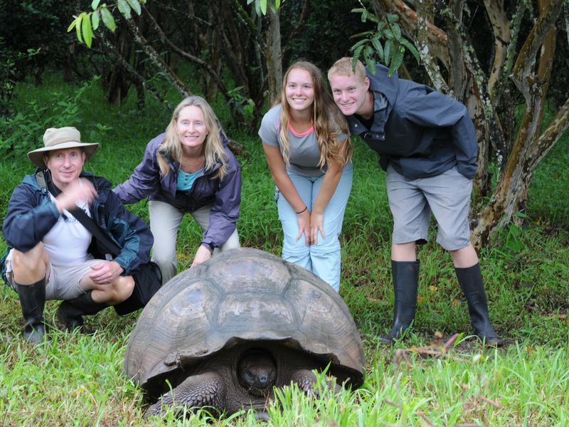 A family of four poses behind a Galapagos Tortoise in the Galapagos Islands.