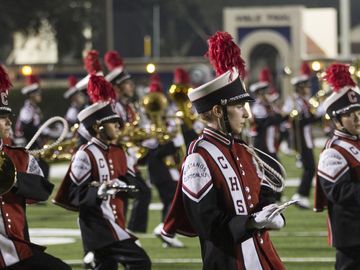 A marching band performs on a football field at night.