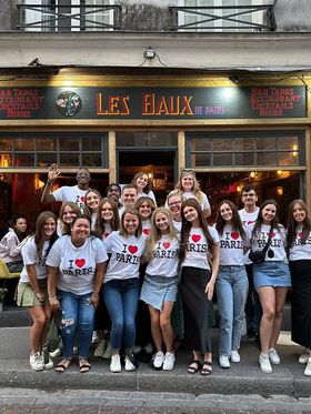 Group of young adults in 'I Love Paris' t-shirts in front of Les Baux de Paris restaurant