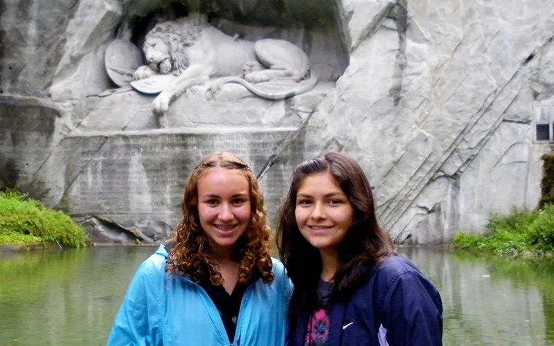 Two teenage girls pose for a photo in front of the Lion Monument, Lucerne, Switzerland.