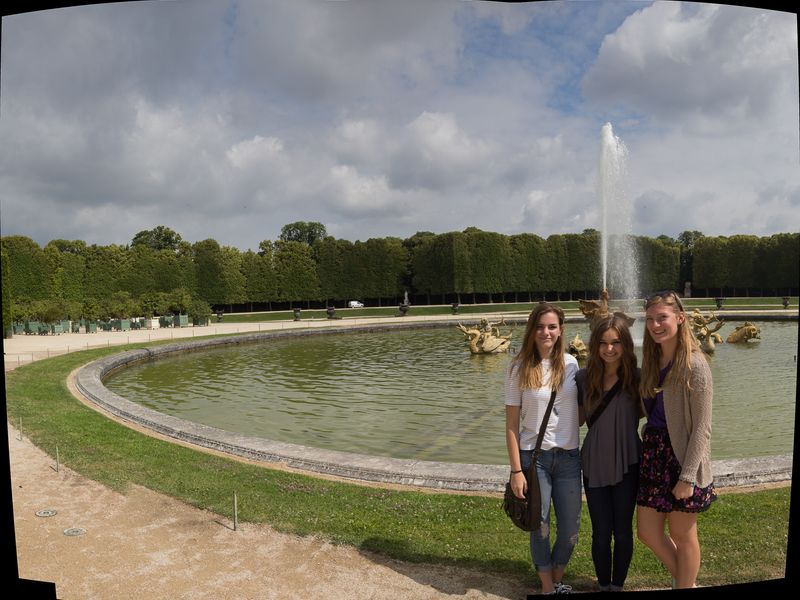 Three young women pose before a fountain at the Palace of Versailles in Paris, France