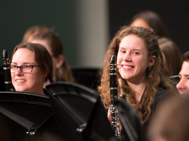 Close up shot of two smiling girls holding clarinets among other musicians.