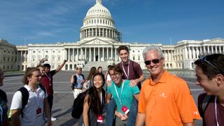 Group of teenagers and young adults posing for a photo with the US Capitol Building in the background.