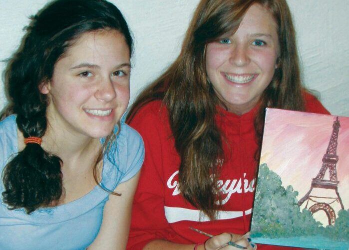 Two teenage girls proudly display a painting of the Eiffel Tower.