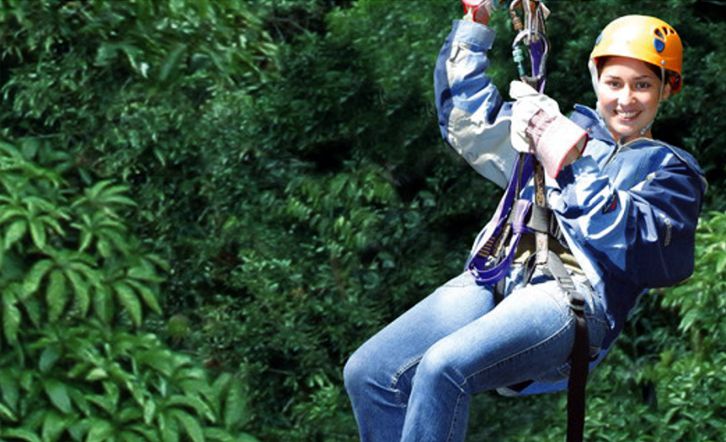 A young woman ziplining through a forest canopy.