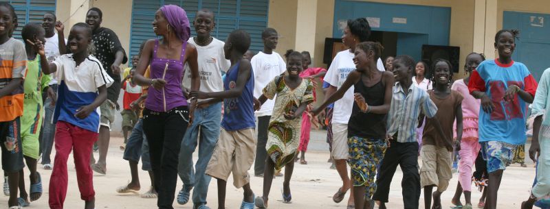 A group of African children and adults joyfully playing outside a building.