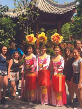 Group of teenagers pose with Chinese performers in traditional costumes.