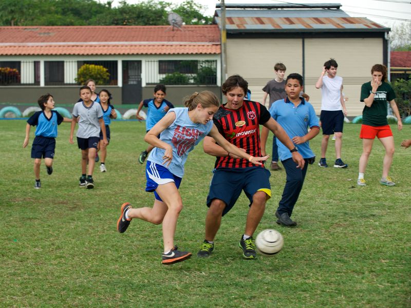 Teenagers playing a game of soccer on a grassy field.