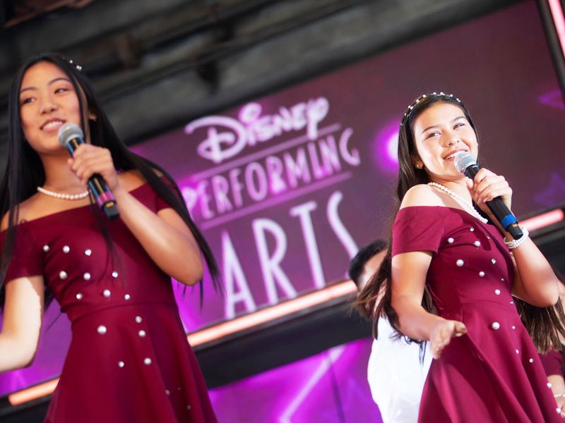 Two teenage girls singing into microphones on a stage.