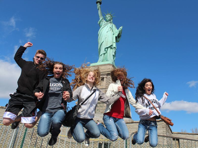 Five teenagers jumping in the air with excitement in front of the Statue of Liberty