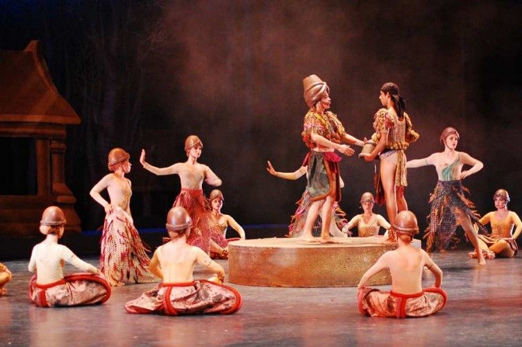 Ballet dancers in earthy costumes perform on stage.