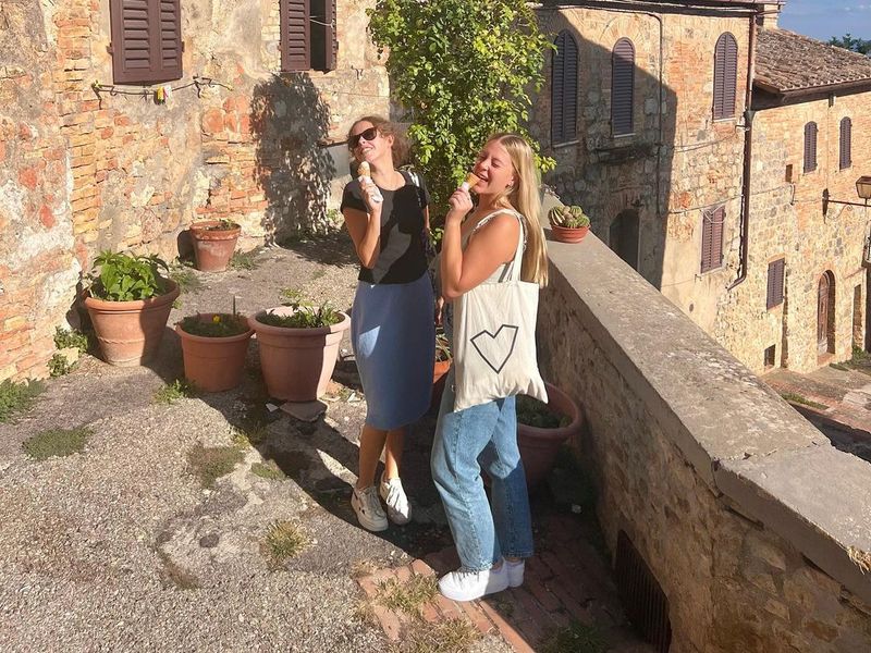 Two young women enjoy gelato in a picturesque Italian village.