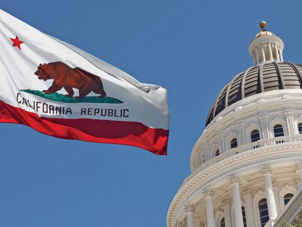 The California State Capitol building with the California state flag waving in the foreground.