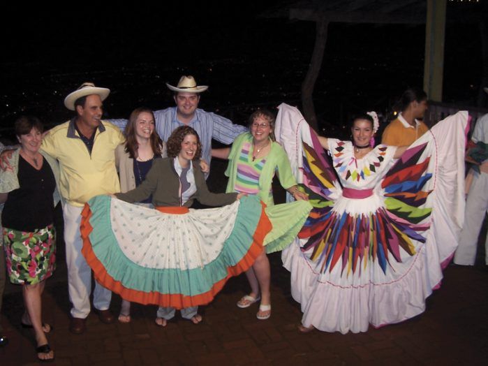 Group photo of adults and young adults in traditional colorful attire, celebrating and smiling.