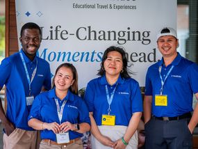 Four young adult WorldStrides representatives smile in front of a promotional banner highlighting life-changing educational travel experiences.