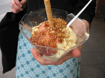 A serving of spaghetti ice cream, a creative dessert where vanilla ice cream is made to look like pasta, topped with strawberry sauce and white chocolate shavings.