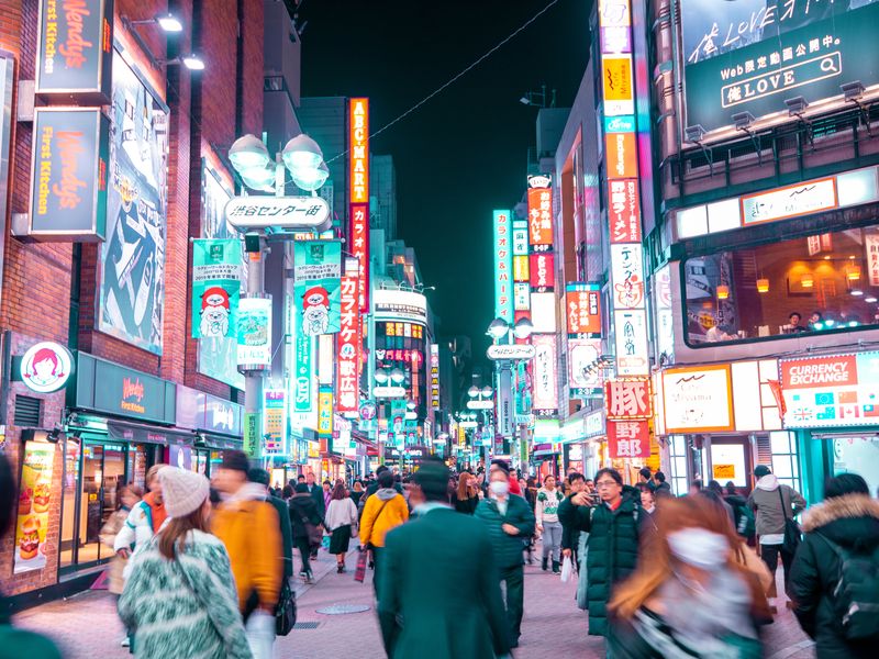 A bustling city street at night with illuminated neon signs and blurred motion of people.