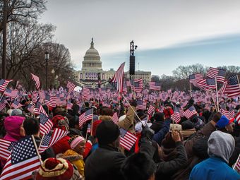 A large crowd of people waving American flags in front of the United States Capitol Building