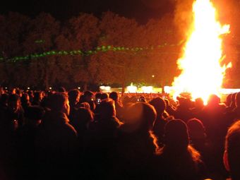 Crowd gathered around a large bonfire at night.