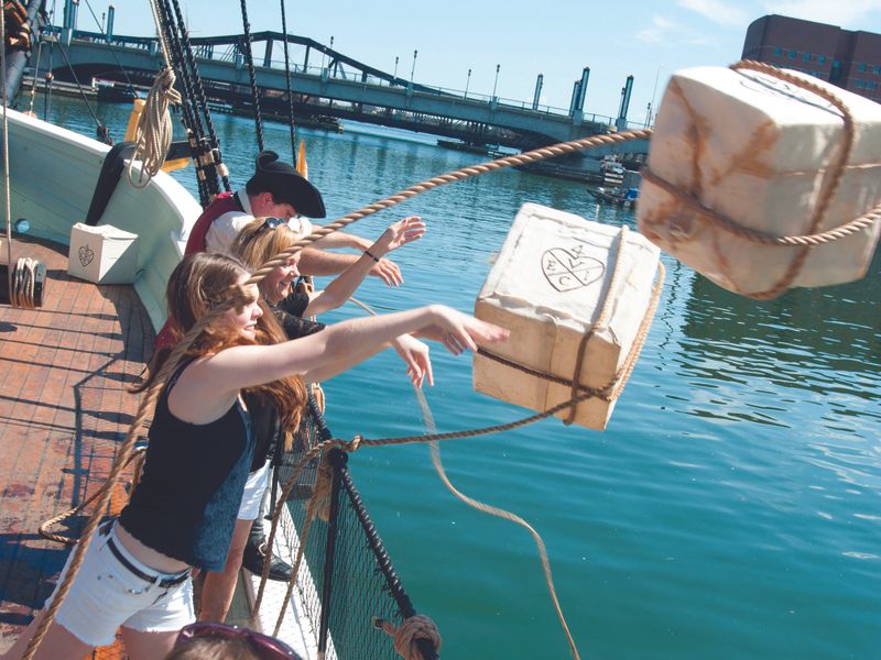 A group of people throw packages off the side of a ship into the water.