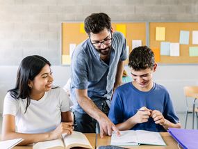 A teacher helps two high school students with their classwork in the classroom. 