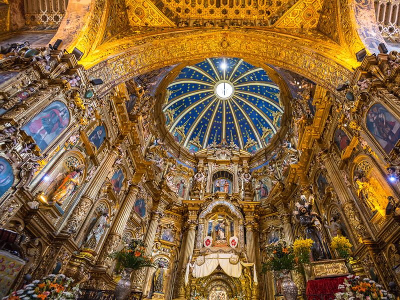 Interior view of an ornate San Francisco Church with gold leaf and a blue-painted dome, located in Quito, Ecuador.