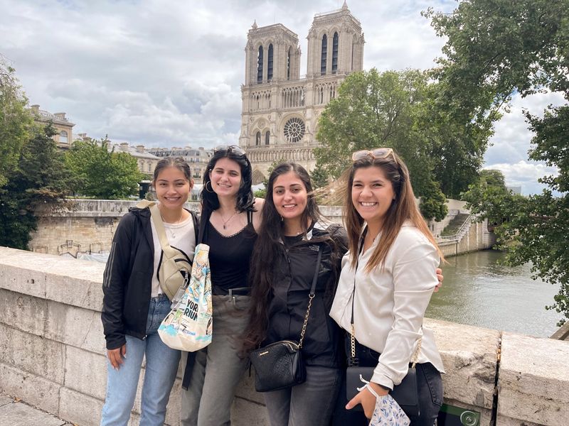 Four young women pose on a bridge with Notre Dame in the background.