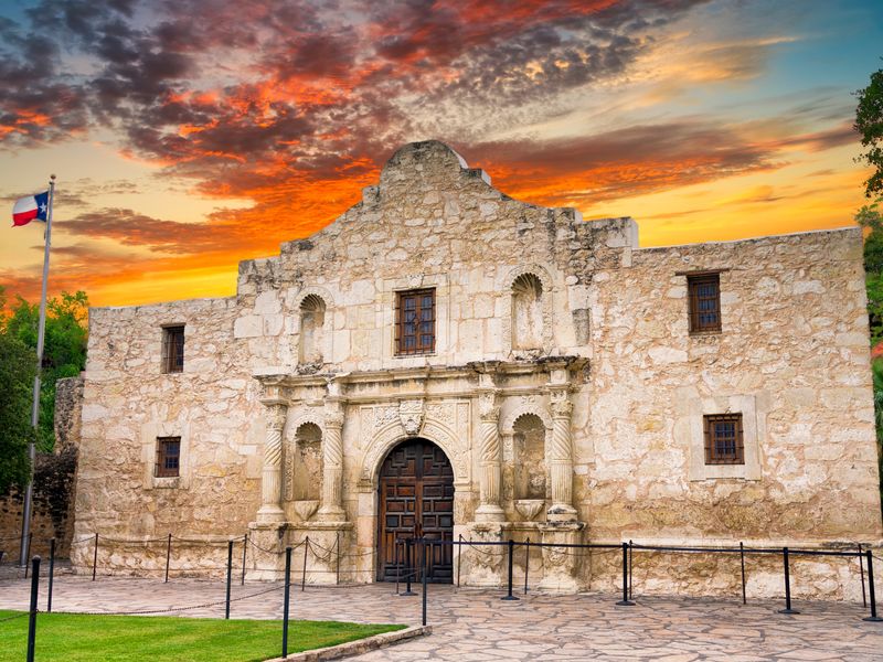 The Alamo at sunset with the Texas flag waving next to it.