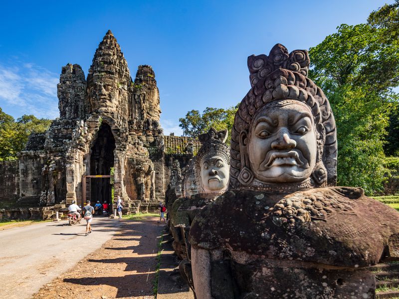 Stone faces at the South Gate entrance to Angkor Thom, Cambodia with tourists on bikes and motorbikes in the distance.