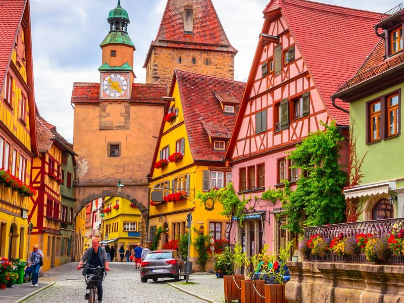 A charming street in Dinkelsbühl, Germany, with colorful half-timbered buildings, a clock tower, and vibrant flower boxes.