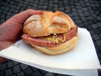 A close-up of a hand holding a Fleischkäse Semmel, a German meat sandwich.