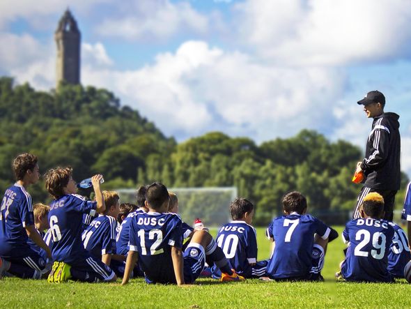 A youth soccer team takes a knee on the field while their coach gives them instructions.