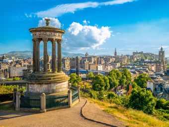 Scenic view of Edinburgh from Calton Hill, featuring the Dugald Stewart Monument in the foreground, and Edinburgh Castle among other landmarks in the distance.