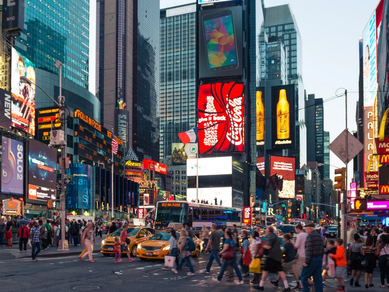 A view of Times Square at dusk with crowds of people and bright billboards.