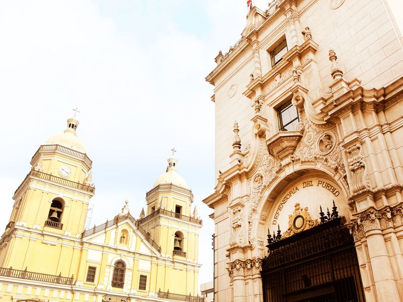 Two historic buildings in Lima, Peru, a yellow church and a tan building with ornate carvings.