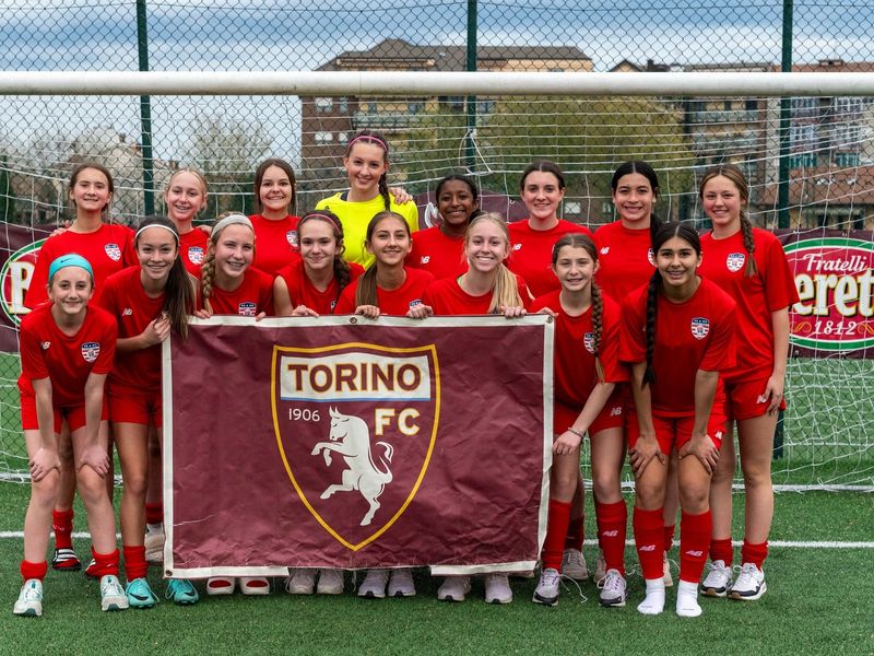 A girls' soccer team in Turin, Italy proudly displays their team banner on a lush green field.