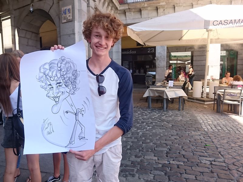 Young man proudly displays a caricature drawing in a city square.